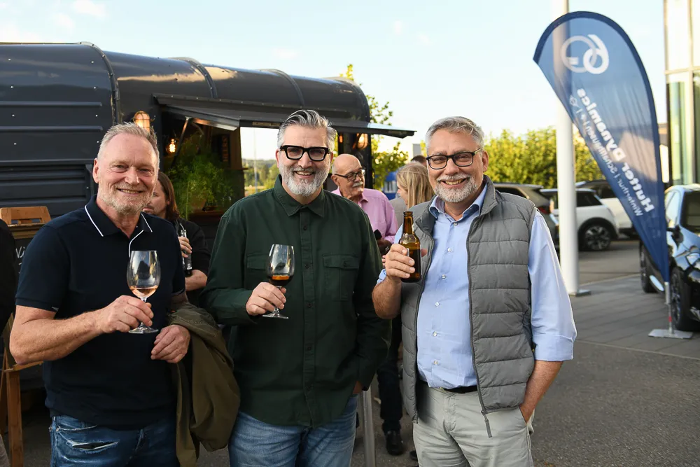 Drei Gäste stossen mit Wein und Bier vor dem Wagen an einem Firmenanlass an
