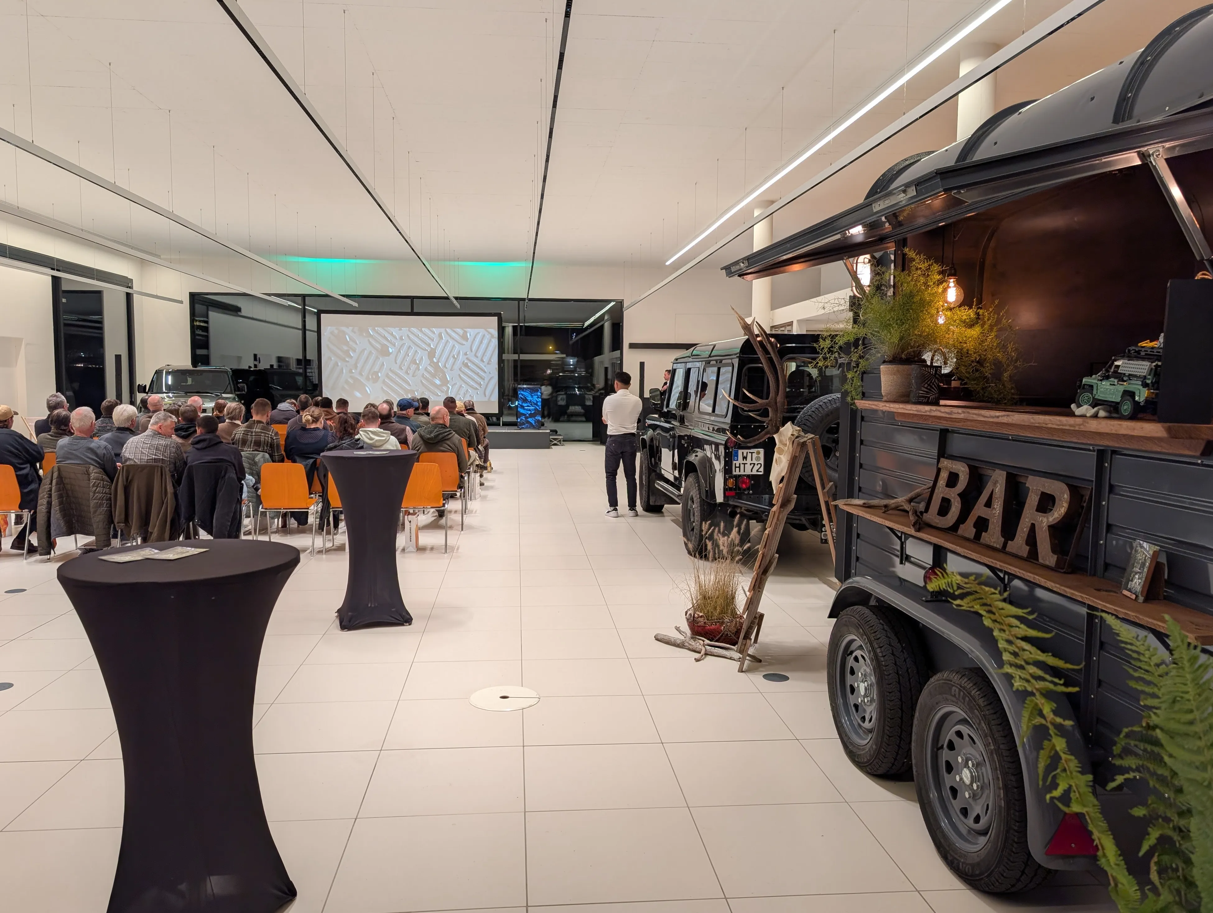 Der Wagen als Bar in einer Autohaus-Halle aufgebaut, im Hintergrund Gäste bei einer Präsentation