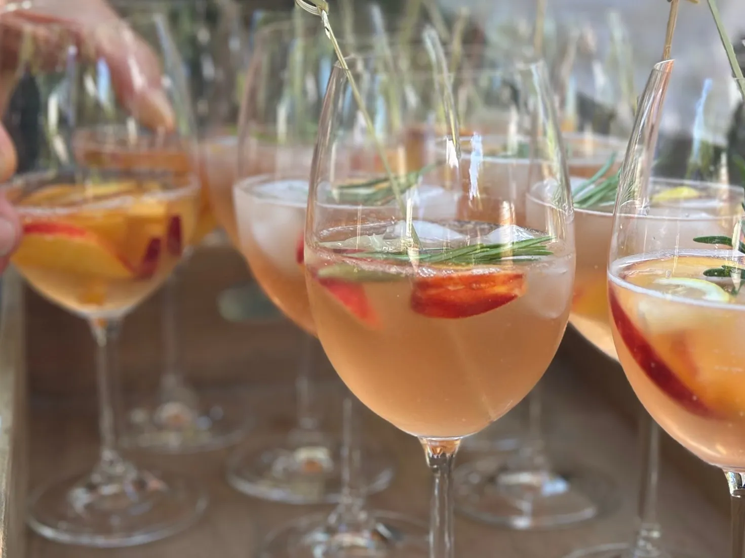 Aperol-Spritz-Cocktails mit Rosmarin-Garnitur auf einem Holztablett, werden gerade ausgeteilt