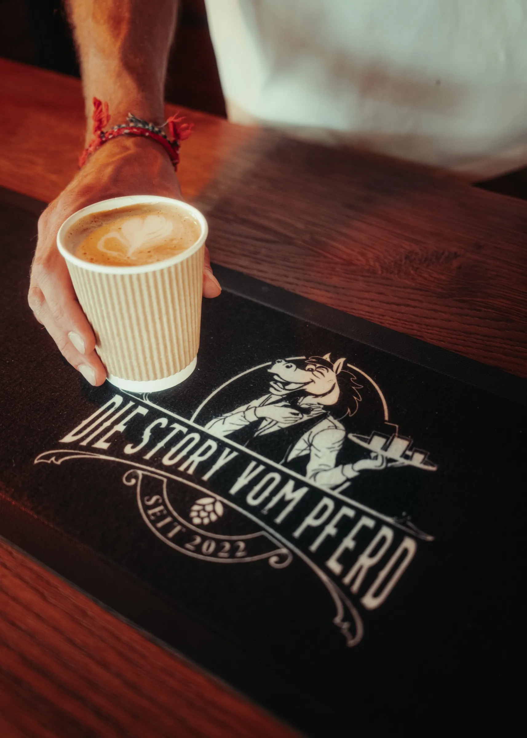 Kaffee mit Latte Art wird auf der Bar-Matte mit dem Logo serviert