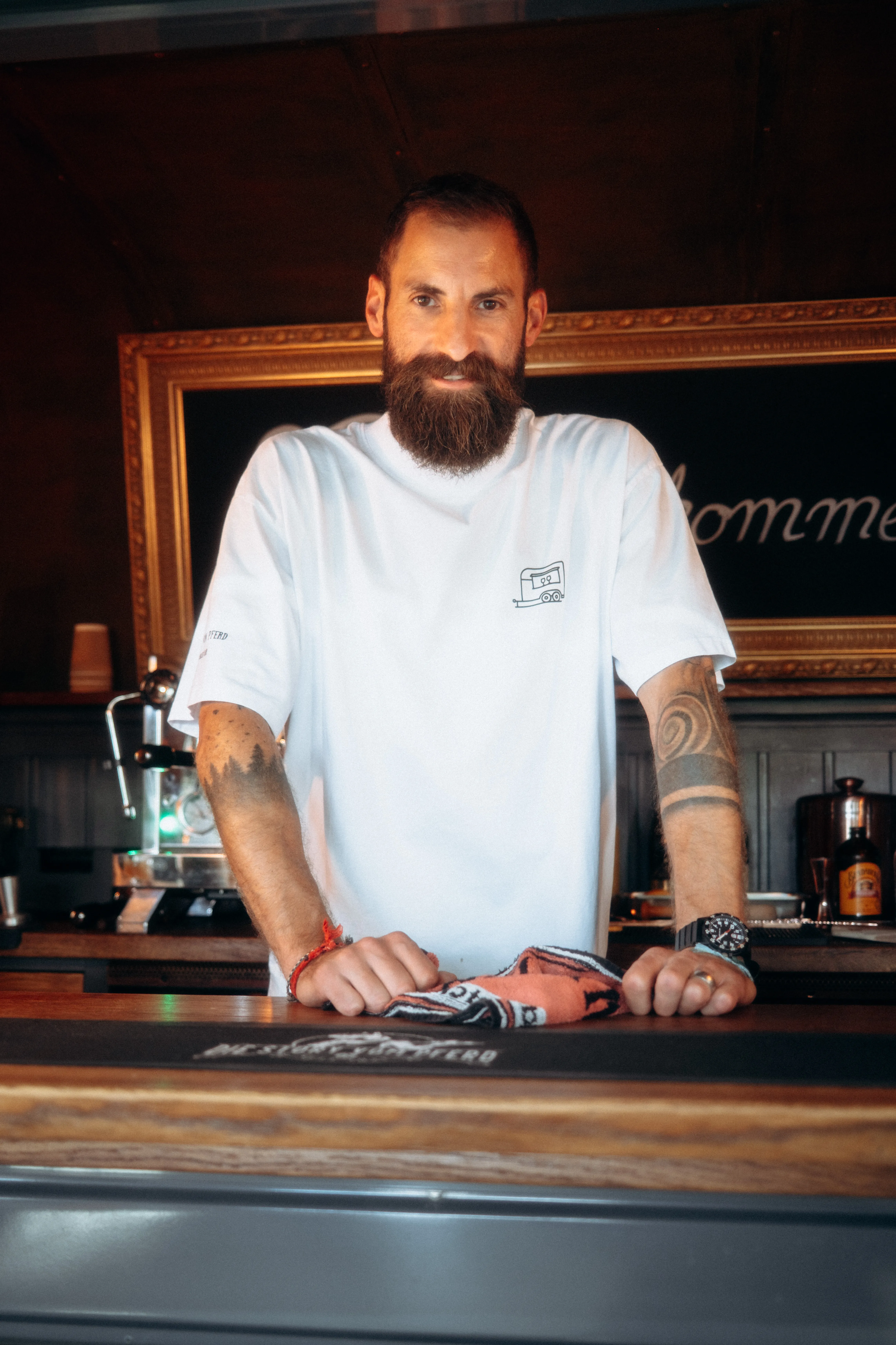 Kim steht hinter der Theke im Wagen, weisses Shirt mit Wagen-Logo, Kreidetafel und Kaffeemaschine im Hintergrund