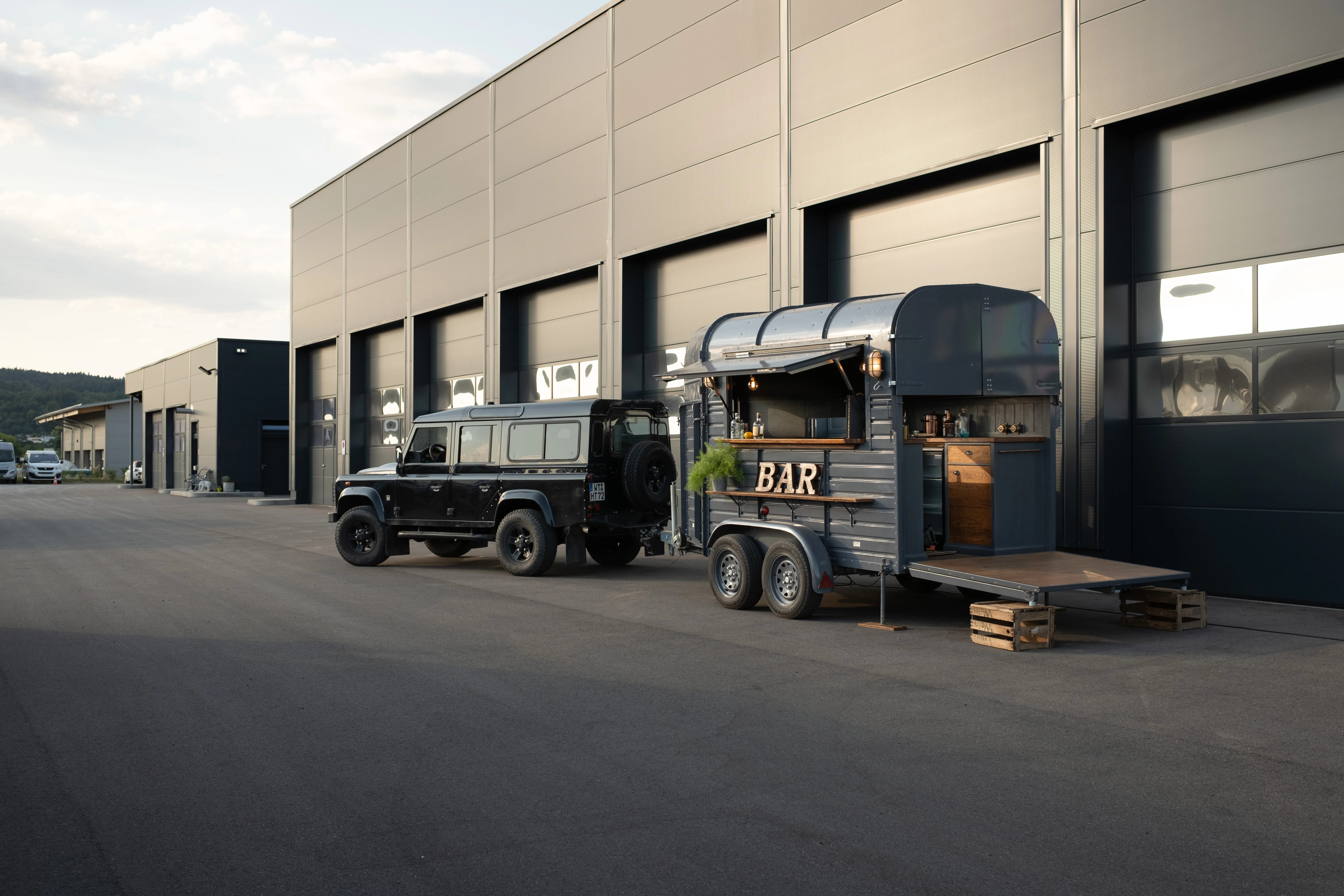 Der Land Rover Defender mit dem Pferdeanhänger vor der Halle, blaue Stunde